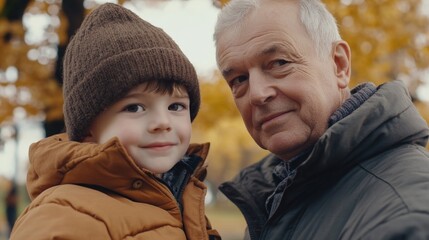 Joyful grandfather and smiling grandson in vibrant autumn park setting with orange and yellow foliage showcasing meaningful intergenerational bond