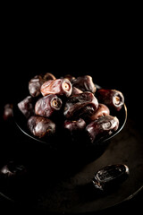 Close-up view of dried dates arranged in a black bowl against a dark background highlighting their rich texture