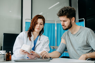 Female doctor checking man blood pressure at clinic and filling patient history.