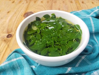 Moringa leaves soup in bowl on wooden table. High angle view setup 