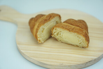 Freshly baked croissant with cheese custard filling cut into two parts on a light brown round cutting board, isolated on a white background