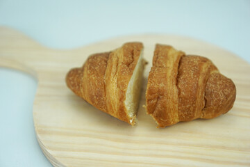 Freshly baked croissants cut into two pieces on a light brown round cutting board, isolated on a white background