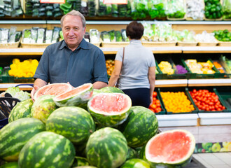 Satisfied man chooses ripe sweet watermelon on grocery store window
