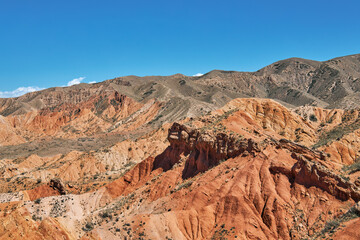 Striking landscape features expansive hills with vibrant hues of red, orange, tan, characteristic of desert environment. terrain is rugged and undulating, natural scene, Fairy Tale canyon, Kyrgyzstan