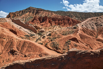 Striking landscape features expansive hills with vibrant hues of red, orange, tan, characteristic of desert environment. terrain is rugged and undulating, natural scene, Fairy Tale canyon, Kyrgyzstan