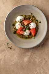 Caprese salad with fresh mozzarella and sliced tomatoes, served with micro greens and pesto sauce on beige background top view. Italian food, text space