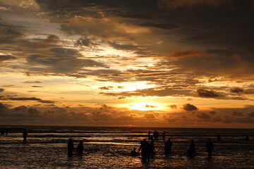 Silhouette people man a woman on the sunset background, mSunset on the tropical beach Seminyak. The tourists watching for beautiful sunset in the sea. Coast of the sea at colorful sunset.