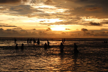 Silhouette people man a woman on the sunset background, mSunset on the tropical beach Seminyak. The tourists watching for beautiful sunset in the sea. Coast of the sea at colorful sunset.