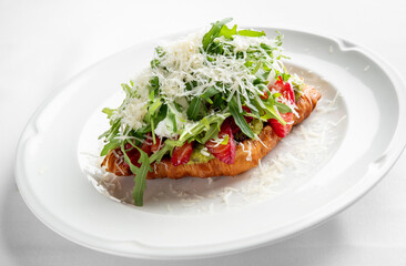 A gourmet croissant topped with fresh arugula, salmon, and grated cheese, presented elegantly on a white plate. Ideal for food photography and culinary delights.