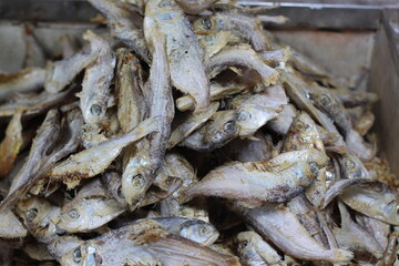 Crispy small fish placed on the stall for sale. Close up of stacked dried anchovies. A pile of dried anchovies displayed in a fish market, Little dried fish in an Asian fish market.