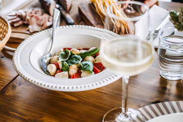 Rustic dining setup with Caprese salad, white wine, and fresh ingredients, showcasing farm-to-table dining and natural elegance