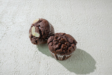 Two of cupcakes on textured white: one chocolate with chocochips and one chocolate with almond slices
