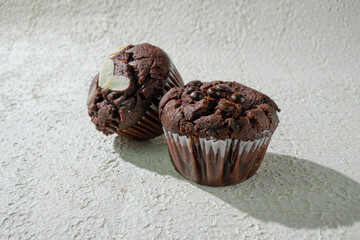 Two of cupcakes on textured white: one chocolate with chocochips and one chocolate with almond slices