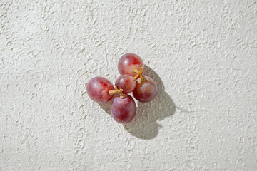 Close up of vibrant red grapes against a textured white background, highlighting their freshness and texture