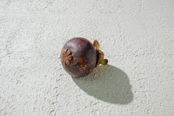 Mangosteen fruit displayed against a textured white background, emphasizing its unique purple rind and freshness