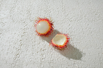 Peeled rambutan revealing its translucent, juicy flesh, set against a textured white background for...