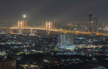 Obraz premium Nightscape view of Skyscrapers with Thotsamarachan Bridge (Rama IX Bridge) crossing Chao phraya river. Beautiful city of Bangkok with bright glowing lights, use it as your Wallpaper, Poster and Space.