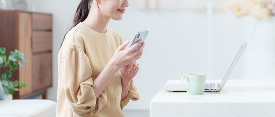 家でパソコンとスマホで仕事する女性