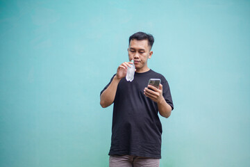 Man holding bottled drink and playing smartphone while walking