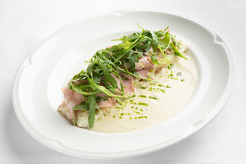 A gourmet dish featuring omelet topped with ham and fresh arugula, accompanied by a creamy sauce. Ideal for culinary and restaurant promotional materials.