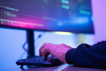Person typing on a keyboard in a dimly lit room with colorful lighting effects during an evening session