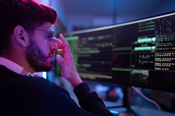 Focused programmer analyzes complex code on dual monitors in modern workspace during nighttime hours