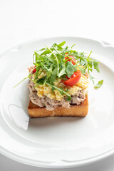 A delicious open-faced sandwich with a toasted slice of bread topped with creamy tuna salad, fresh cherry tomatoes, and a sprinkle of arugula. Perfect for a light meal or snack.