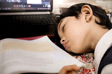 Southeast Asian boy fallen asleep while doing his homework on a computer at home after school