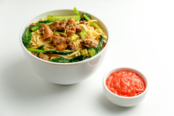 Chicken noodle or in Indonesian called mie ayam with vegetable, chopped chicken, chicken foot, isolated in white background. This food usually serve with chili or spicy red sauce