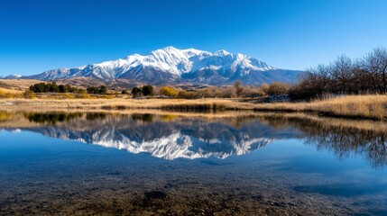 Naklejka premium Snow-Capped Mountain Range Reflected in Tranquil Lake, Serene Landscape, Majestic Peaks, Mirror-Like Water Surface, Crisp Atmosphere