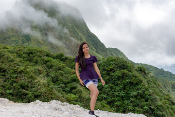 Naklejka premium Portrait of a beautiful young Filipina woman against the background of a volcano covered with smog and clouds