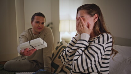 Caring husband presenting gift to excited beautiful wife in apartment closeup.