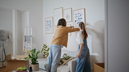 Married couple hanging artwork on wall new home. Spouses decorating living room