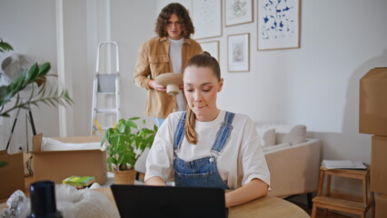 Focused woman working laptop in modern home. Lady surrounded by moving boxes
