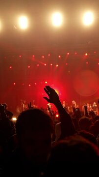 Vertical shot of concert front row crowd cheering hands in air slow motion night light rock rap concert People cheer move lift their hands, doing peace victory hand sign gesture and jumping 