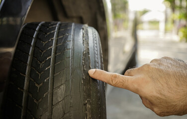 Close-up of man's finger pointing at worn car tire with bald tread from use. Car maintenance...