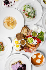 A vibrant breakfast spread featuring eggs, crispy bacon, sausages, fresh vegetables, and assorted breads, complemented by yogurt and a fruity dessert. Perfect for food lovers and restaurants.
