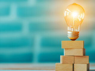 A glowing light bulb sits atop wooden blocks against a blue background, symbolizing creativity and innovation.