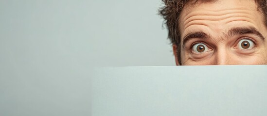 Smiling middle-aged businessman with curly brown hair peeking over empty light blue sign, expressing curiosity and engagement in studio setting