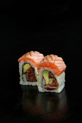 Close-up of two sushi rolls filled with avocado, salmon, and other fresh ingredients, topped with microgreens, presented on a black background for a refined, minimalist look.