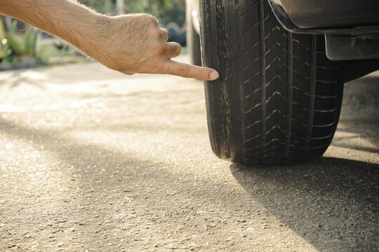 A man's hand points to a tire with bald and worn tread. Car maintenance concept.