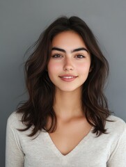 Fototapeta premium Young woman with long dark hair and natural makeup smiling against soft grey background capturing beauty and tranquility in portraiture