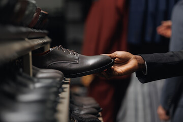 Closeup hand of African American businessman in shirt and suit choosing shoes to match trousers in mens store