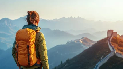 Fotobehang successful woman hiker with orange backpack enjoying breathtaking sunrise views on Great Wall of China surrounded by mountainous landscape © The 2R Artificiality