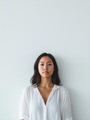 Confident middle-aged woman in white blouse standing against minimalistic light gray wall, ideal for advertising or branding concepts with ample copyspace.