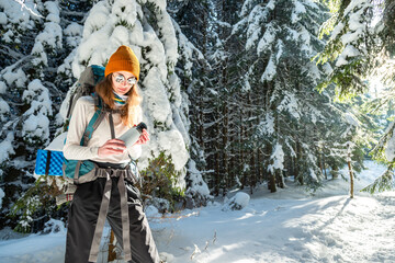Happy Young Female Backpacker Hiking In The Winter Woods With Hot Tea From Insulated Drink...