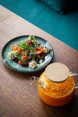 Sea buckthorn tea in a brewed teapot and salad with strachatella, salmon and salmon on a wooden table in the restaurant