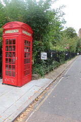 Obraz premium Iconic red telephone booth beside a lush street in London