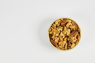 Assorted nuts in a stoneware container with a straw basket, on a white background. Almonds, Walnuts, Cashews and Chestnuts