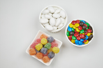 Jelly candies and dipped chocolates, in various bright and vivid colours, in suitable containers, on a white background.